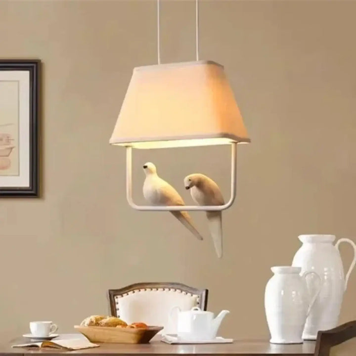 Suspension luminaire lumibird avec abat-jour beige en tissu et cadre blanc minimaliste, deux colombes sculptées suspendues