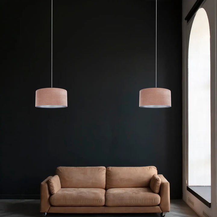 Deux suspensions luminaires cylindriques en tissu rose blush style moderne chic suspendues devant un mur sombre
