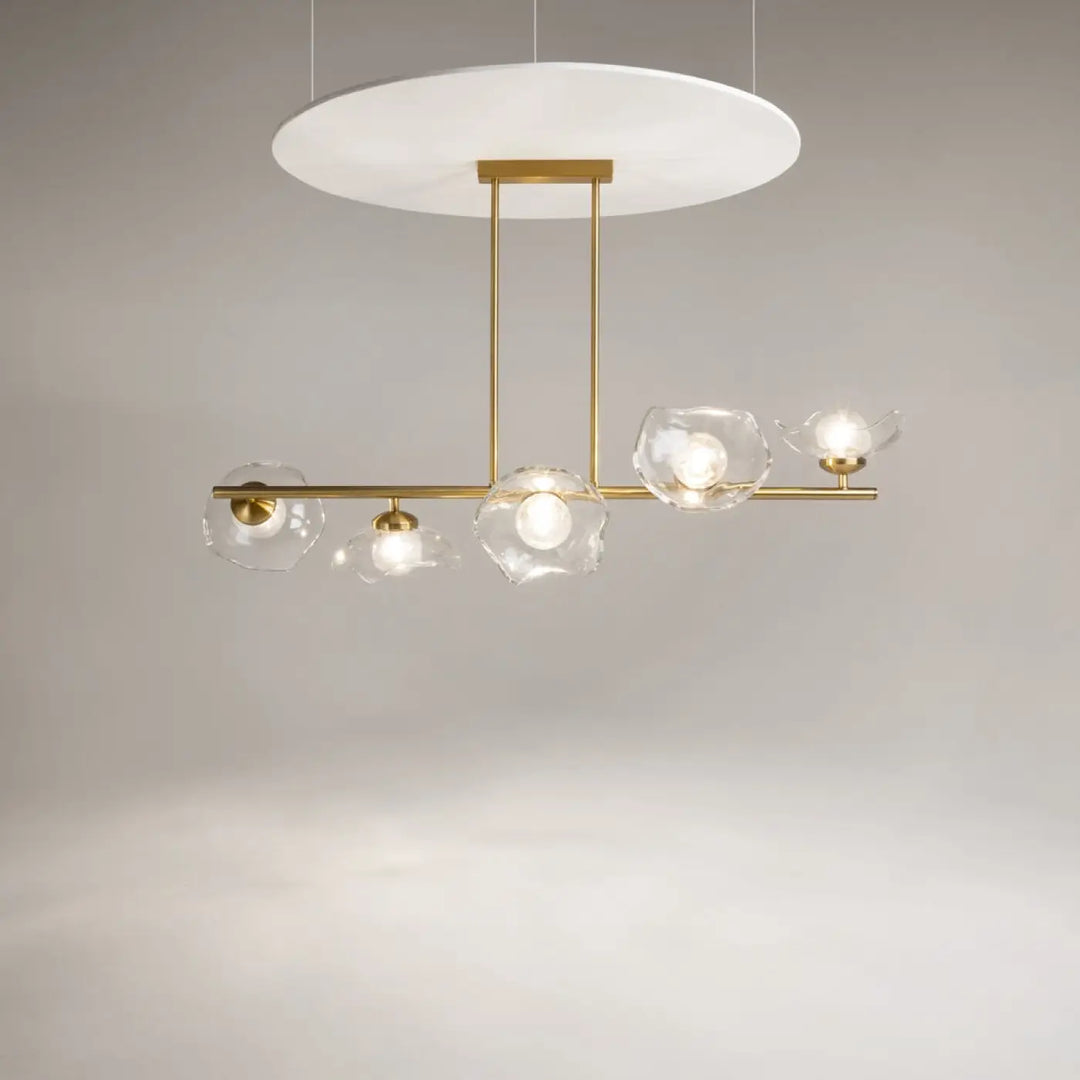 Suspension luminaire miracle avec barre dorée et cinq diffuseurs en verre fleur clair autour d’un diffuseur circulaire blanc