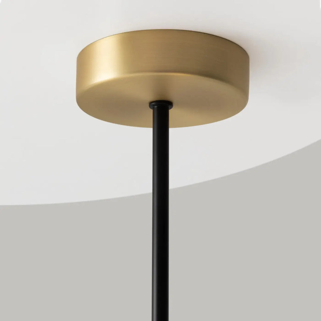 Suspension luminaire nostalgia linéaire avec base en laiton brossé, tige en acier noir au-dessus d’une table en verre opalin
